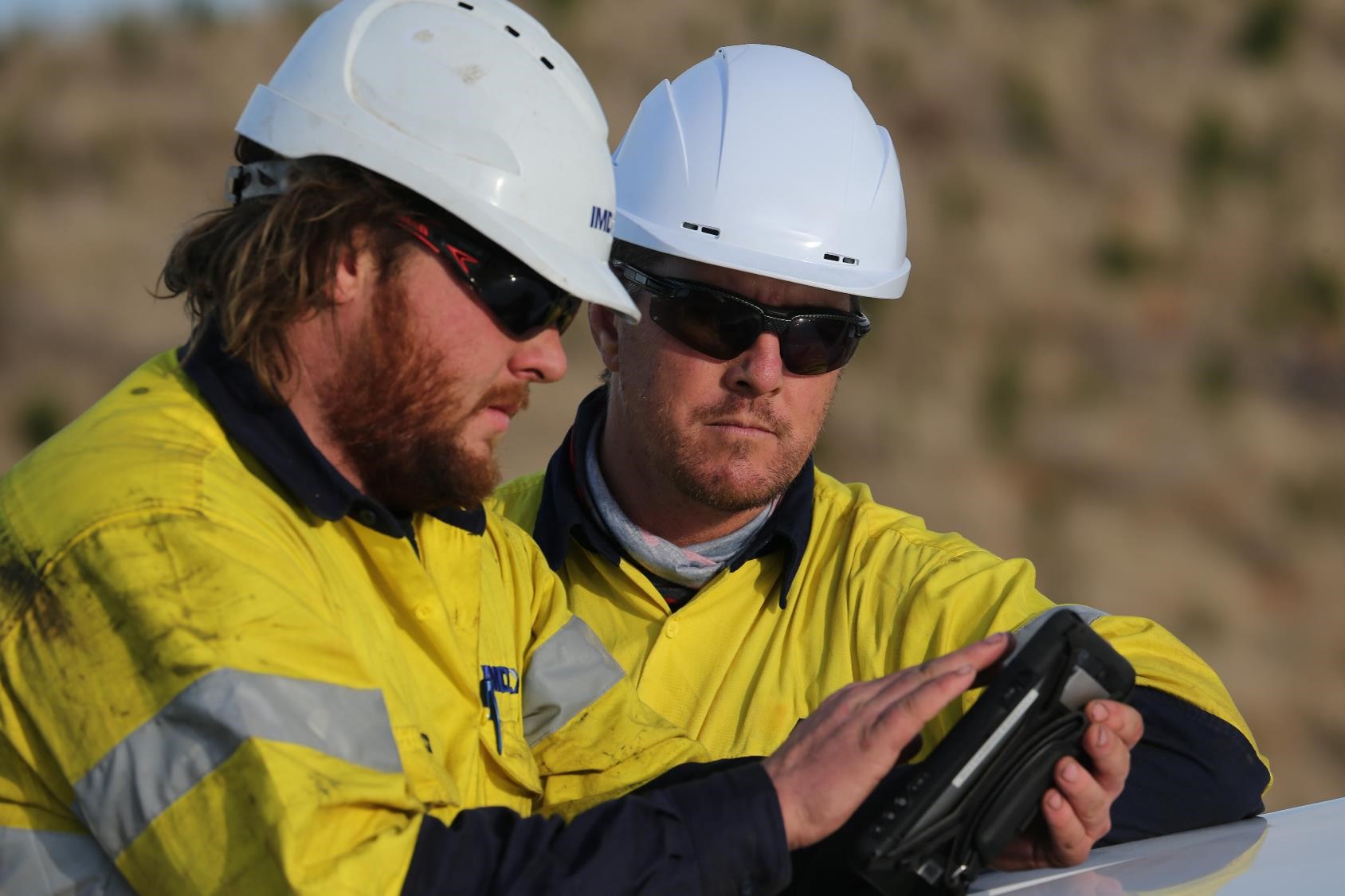 two men in protective suit and helmet looking at a tablet